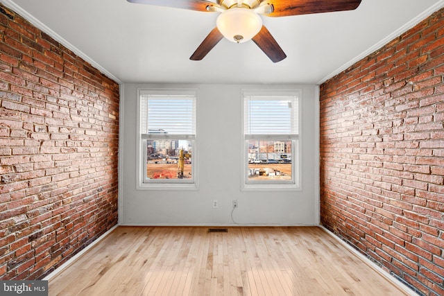 spare room featuring ornamental molding, brick wall, and light hardwood / wood-style flooring