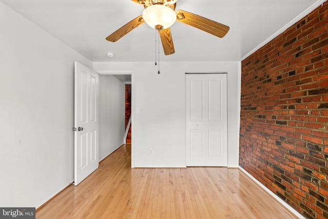 unfurnished bedroom featuring ceiling fan, a closet, brick wall, and light wood-type flooring