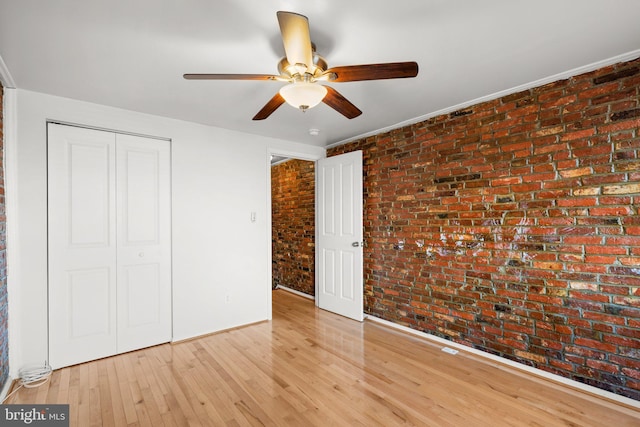 unfurnished bedroom with ceiling fan, light hardwood / wood-style floors, brick wall, and a closet