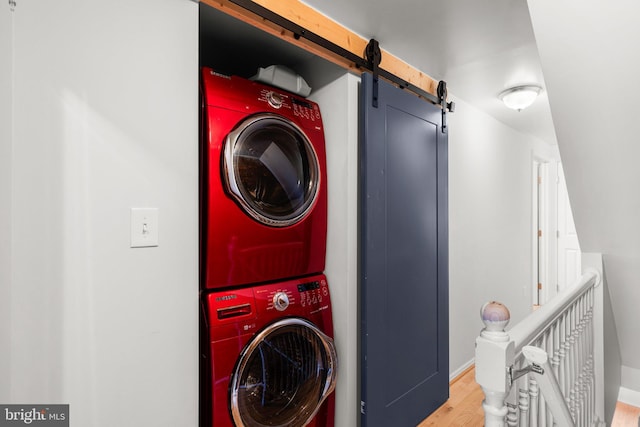 washroom featuring hardwood / wood-style floors, a barn door, and stacked washer / dryer