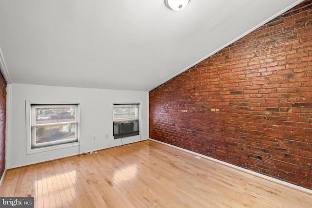 unfurnished living room featuring cooling unit, brick wall, vaulted ceiling, and light wood-type flooring