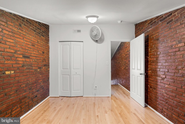 unfurnished bedroom featuring light hardwood / wood-style floors, brick wall, and a closet