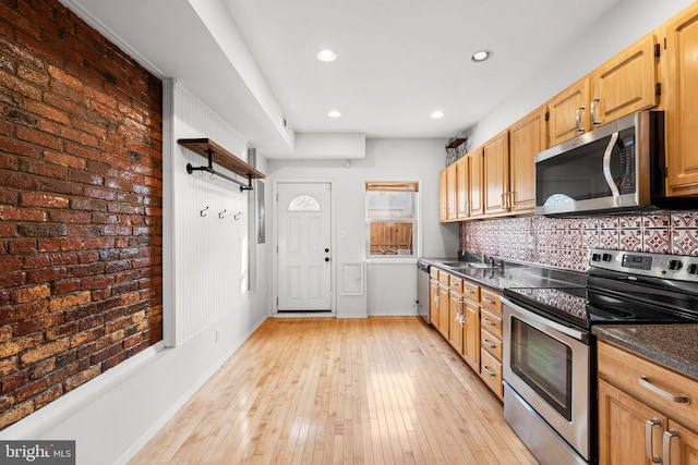 kitchen featuring dark stone counters, sink, decorative backsplash, light wood-type flooring, and appliances with stainless steel finishes