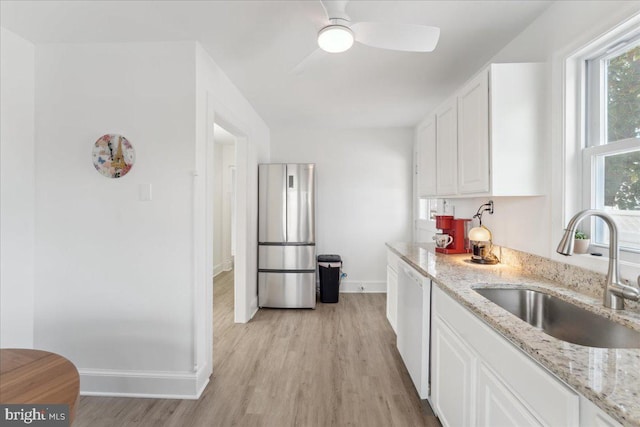 kitchen featuring white cabinetry, sink, stainless steel fridge, white dishwasher, and light stone countertops