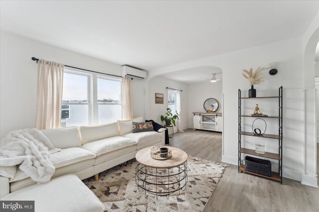 living room featuring ceiling fan, light wood-type flooring, a wall mounted AC, and a water view