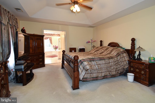 bedroom with a raised ceiling, ensuite bath, ceiling fan, and light carpet