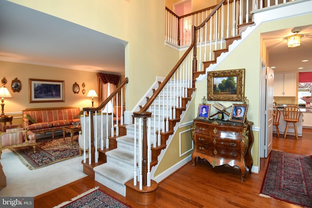 staircase featuring a towering ceiling, hardwood / wood-style flooring, and crown molding