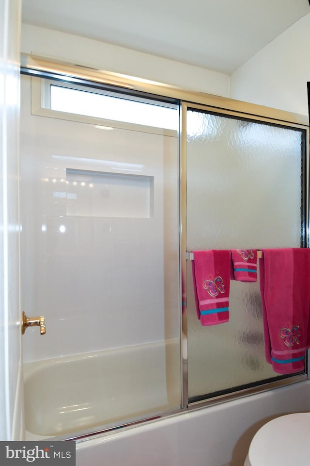 bathroom featuring toilet and combined bath / shower with glass door