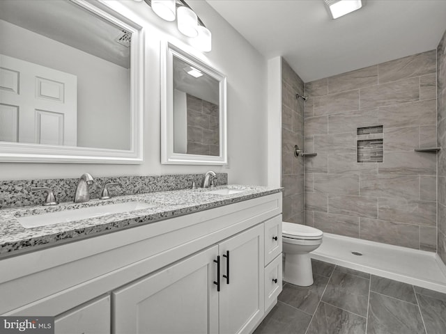 bathroom featuring toilet, a tile shower, and vanity