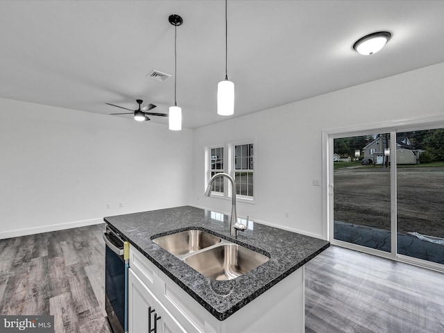 kitchen featuring dark stone counters, white cabinets, hardwood / wood-style floors, hanging light fixtures, and an island with sink