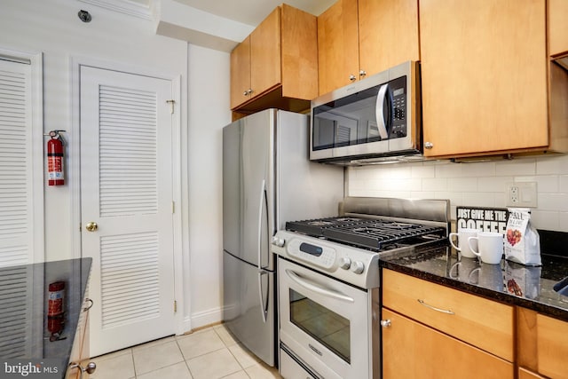 kitchen with dark stone counters, appliances with stainless steel finishes, light tile patterned floors, and backsplash