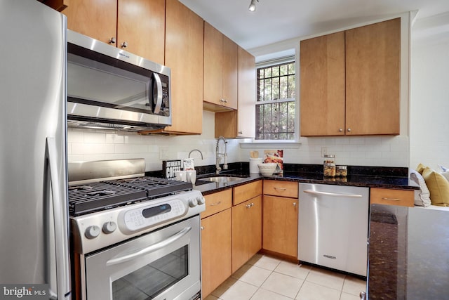 kitchen with stainless steel appliances, dark stone countertops, a sink, and decorative backsplash