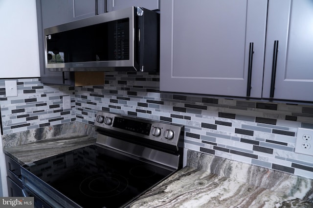 kitchen with appliances with stainless steel finishes, backsplash, gray cabinets, and dark stone counters