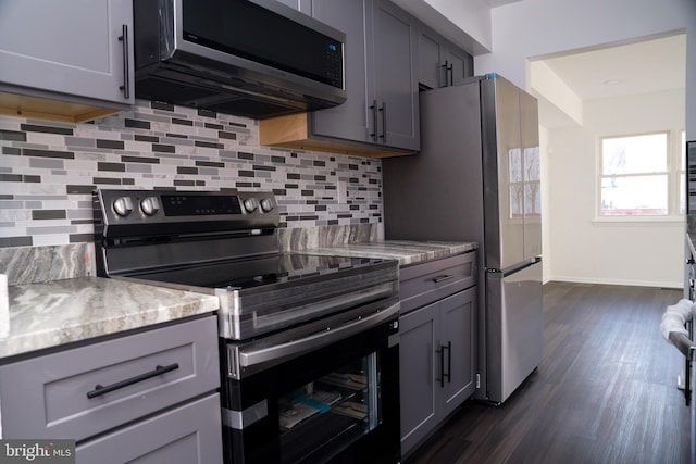 kitchen with gray cabinetry, light stone countertops, backsplash, and appliances with stainless steel finishes