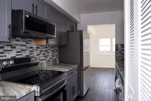 kitchen featuring light stone countertops, dark hardwood / wood-style flooring, backsplash, gray cabinetry, and stainless steel appliances