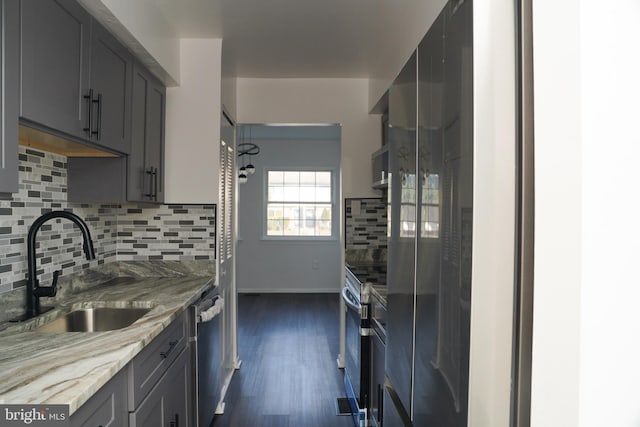 kitchen with gray cabinetry, sink, light stone counters, backsplash, and appliances with stainless steel finishes