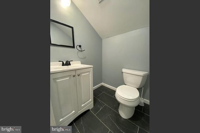 bathroom with tile patterned flooring, vanity, vaulted ceiling, and toilet