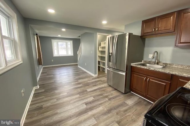 kitchen featuring stainless steel fridge with ice dispenser, light wood-type flooring, black electric range oven, and sink