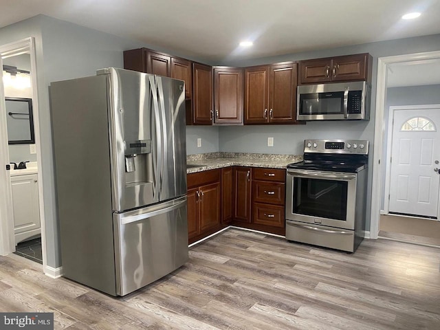 kitchen with dark brown cabinetry, light stone counters, light hardwood / wood-style flooring, and appliances with stainless steel finishes