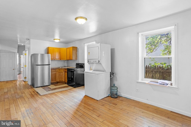 kitchen featuring black range with electric stovetop, sink, stacked washer and dryer, light hardwood / wood-style floors, and stainless steel refrigerator