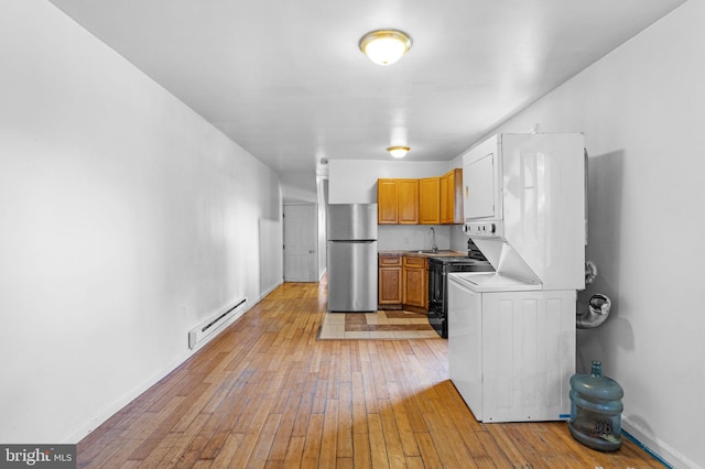 laundry room featuring stacked washer and dryer, light wood-type flooring, a baseboard radiator, and sink