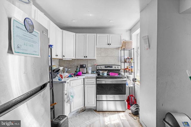 kitchen featuring white cabinets, decorative backsplash, light wood-type flooring, and stainless steel appliances