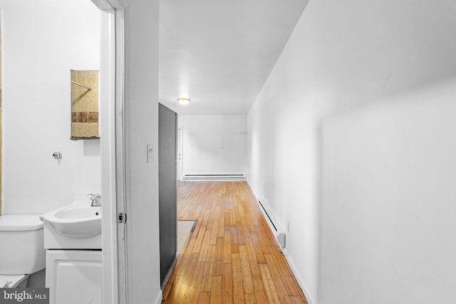 hallway with hardwood / wood-style flooring, baseboard heating, and sink