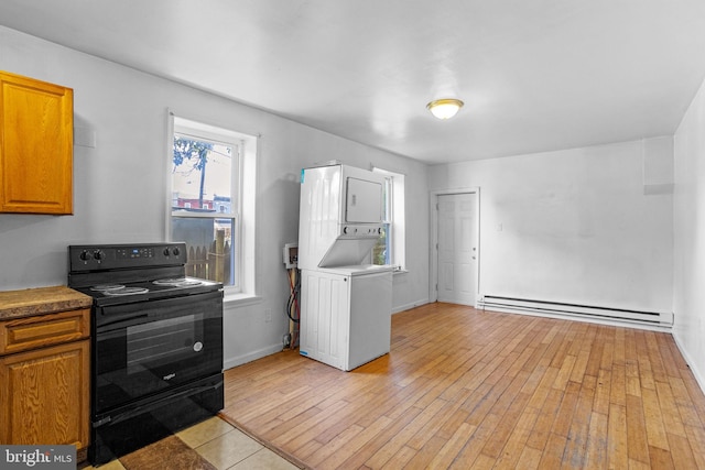 kitchen with black electric range oven, light hardwood / wood-style floors, stacked washer and clothes dryer, and a baseboard heating unit