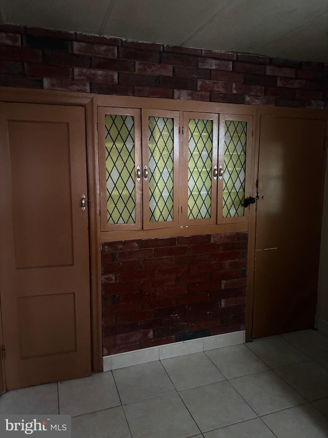 foyer entrance with light tile patterned flooring and brick wall