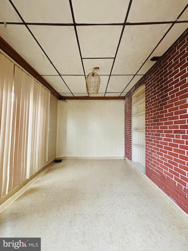 unfurnished room featuring a paneled ceiling and brick wall