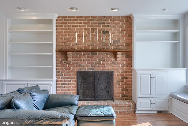 living room featuring a fireplace, crown molding, built in features, and hardwood / wood-style flooring