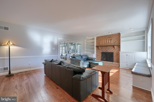 living room featuring built in shelves, wood-type flooring, and a brick fireplace