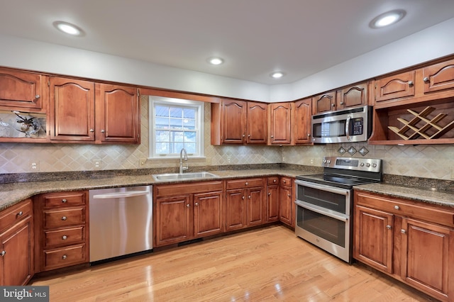 kitchen with sink, dark stone countertops, light wood-type flooring, appliances with stainless steel finishes, and tasteful backsplash