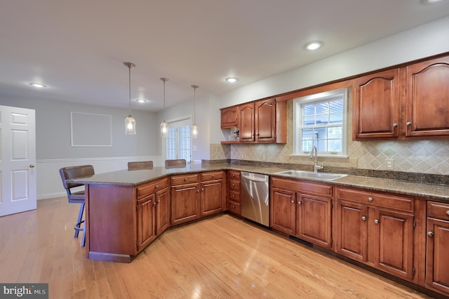 kitchen with kitchen peninsula, stainless steel dishwasher, sink, pendant lighting, and light hardwood / wood-style floors