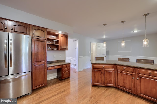 kitchen with dark stone counters, hanging light fixtures, stainless steel fridge, built in desk, and light hardwood / wood-style floors