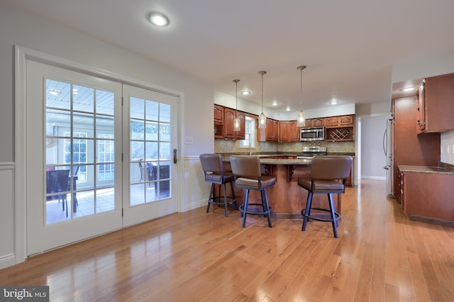 kitchen with kitchen peninsula, appliances with stainless steel finishes, light wood-type flooring, tasteful backsplash, and decorative light fixtures