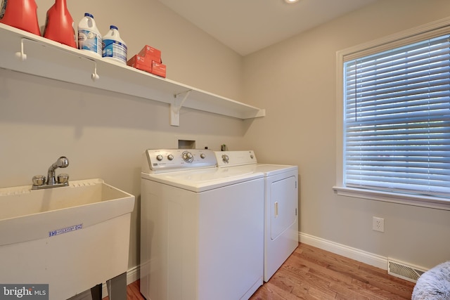 laundry area featuring washing machine and dryer, a healthy amount of sunlight, sink, and light hardwood / wood-style floors