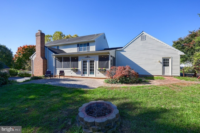 back of house with a sunroom, an outdoor fire pit, a patio, and a lawn