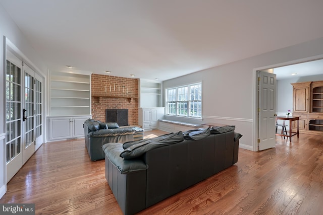 living room featuring built in features, light hardwood / wood-style floors, french doors, and a brick fireplace