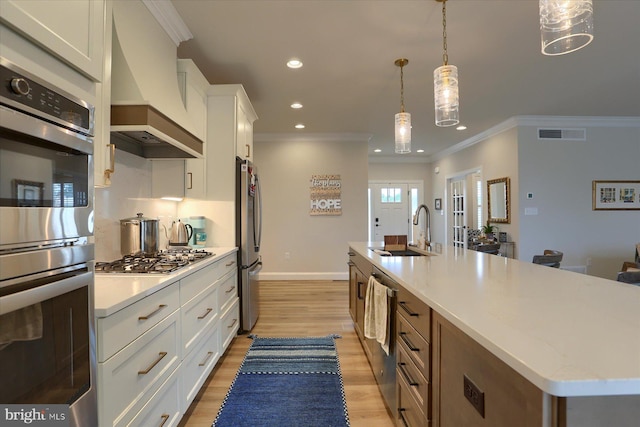 kitchen featuring premium range hood, a large island with sink, white cabinets, hanging light fixtures, and stainless steel appliances