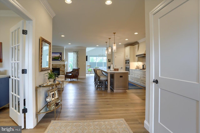 kitchen featuring custom exhaust hood, hanging light fixtures, light wood-type flooring, an island with sink, and a kitchen bar