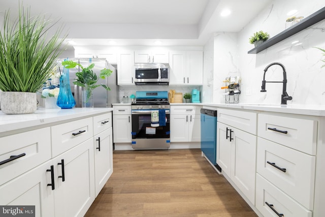 kitchen with backsplash, light hardwood / wood-style flooring, white cabinets, and appliances with stainless steel finishes