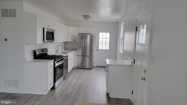 kitchen with stainless steel appliances, light hardwood / wood-style floors, white cabinets, and sink