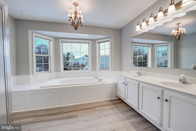 bathroom featuring a wealth of natural light, an inviting chandelier, a relaxing tiled tub, and hardwood / wood-style flooring