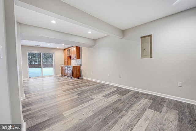 unfurnished living room with beamed ceiling, electric panel, and light hardwood / wood-style flooring