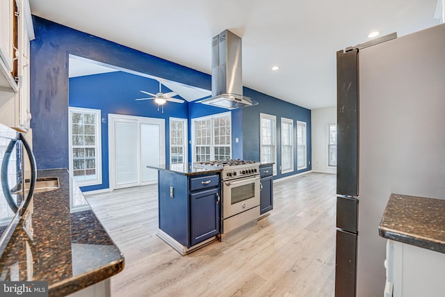 kitchen with blue cabinets, white cabinets, wall chimney range hood, and appliances with stainless steel finishes