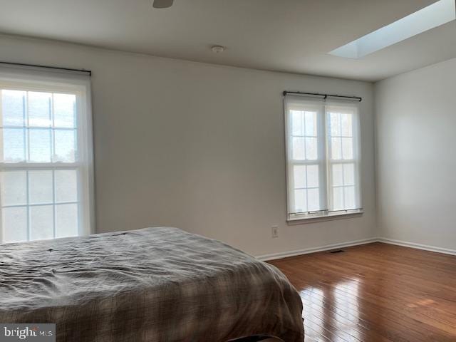 bedroom with multiple windows, a skylight, and hardwood / wood-style flooring