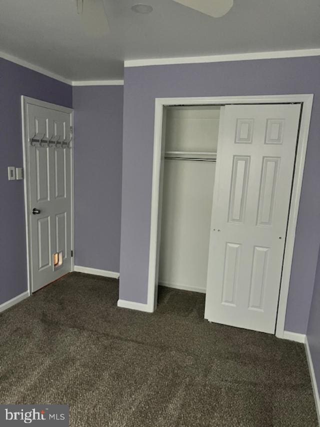 unfurnished bedroom featuring dark colored carpet, crown molding, and a closet