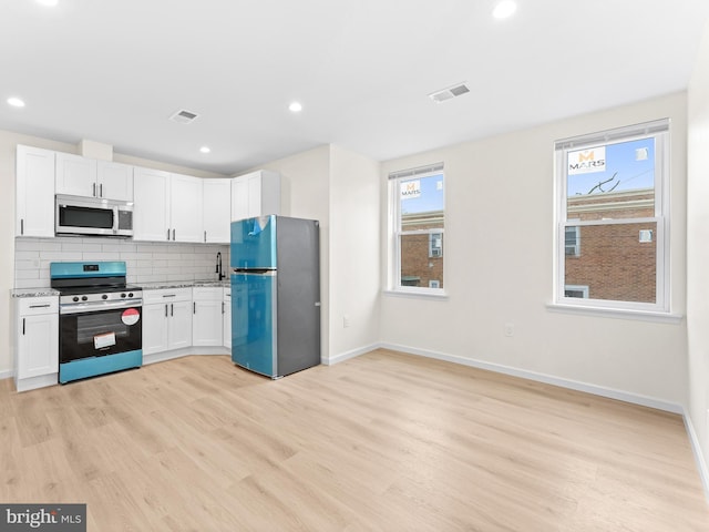 kitchen featuring backsplash, light stone countertops, light hardwood / wood-style floors, white cabinetry, and stainless steel appliances