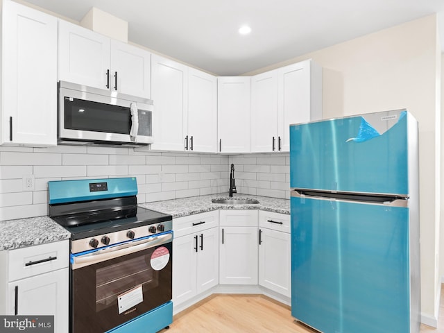 kitchen with backsplash, white cabinets, sink, light stone counters, and stainless steel appliances